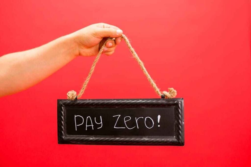 A hand holding a small chalkboard sign that says "PAY ZERO!" against a bright red background, symbolizing the benefits of changing spending habits to eliminate debt.