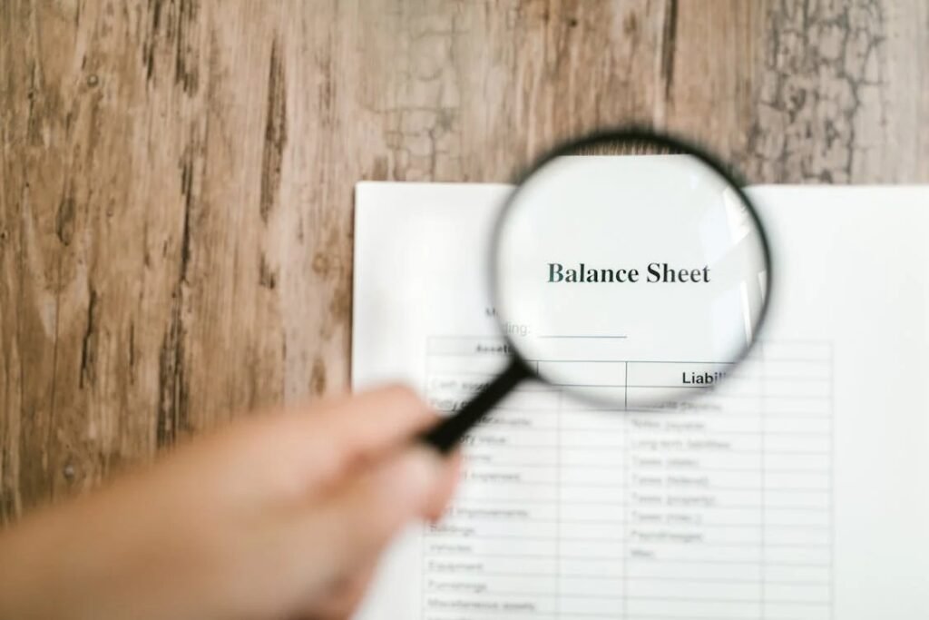 A close-up image of a printed balance sheet being examined through a magnifying glass, symbolizing attention to financial details and the importance of reviewing documents related to investment gifts.