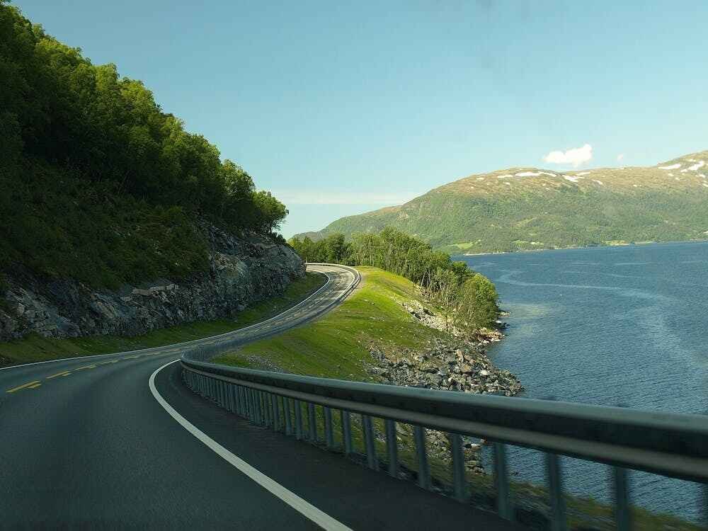 "Scenic road winding along the shore, with lush greenery on one side and a calm body of water on the other, creating a peaceful and picturesque landscape."