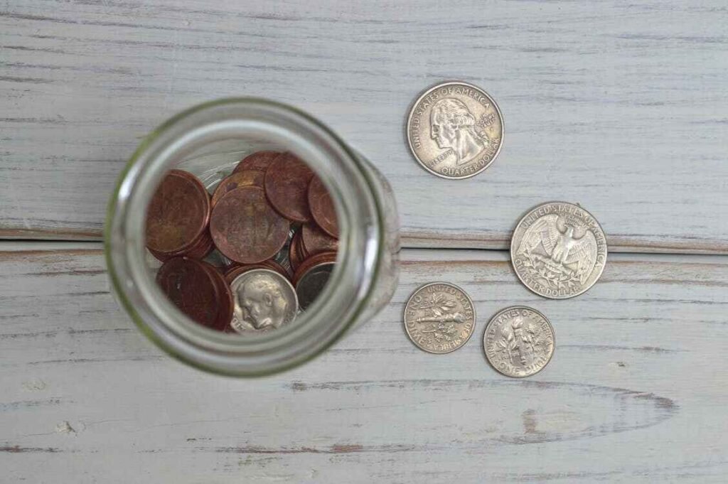 A jar is placed on a table, and some cents are in the jar and some are on the table, showing a jar trick to save money, which is an important budgeting scenario for high school students.