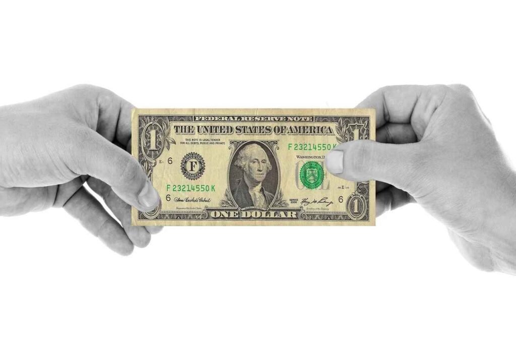 "Two hands exchanging a one-dollar bill, symbolizing the exchange and value of money. This can be tied to the psychology of saving money, reflecting the importance of understanding how money flows and the impact of mindful financial decisions."