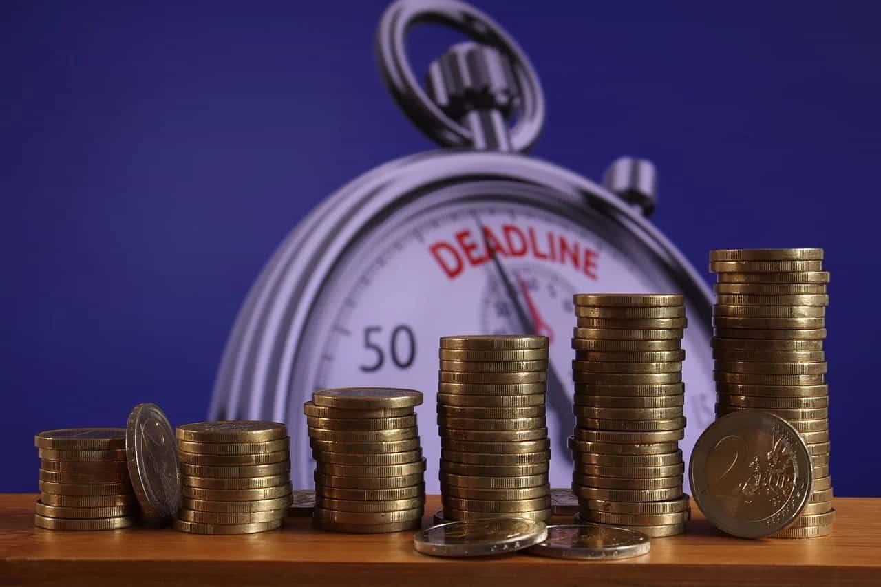 "Stacks of coins on a wooden surface with a backdrop of a stopwatch marked with 'DEADLINE,' symbolizing the importance of managing finances to avoid debt collection and its associated pressures."