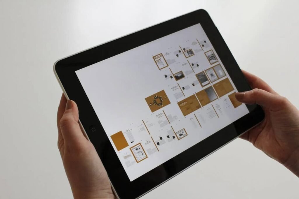 "A person holding a tablet displaying multiple pages of digital documents, possibly related to a project or design layout. The screen shows a collection of content with organized sections in a clean, minimalistic style. This image highlights the convenience and importance of using technology, which can be enhanced by the best budgeting apps for teens to manage their personal finances, track expenses, and stay organized."