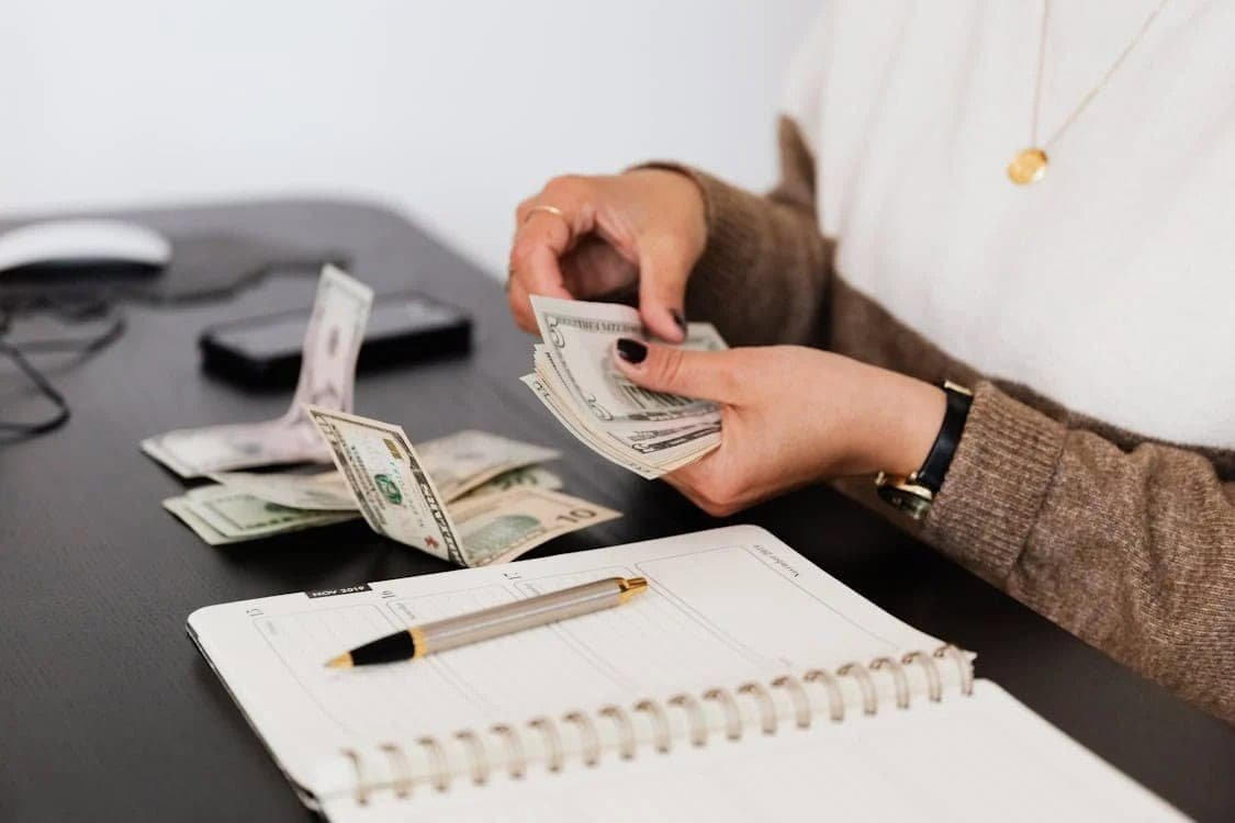 A person counting cash at a desk with a planner, reinforcing that the first priority in your budget should be thoughtful money management.