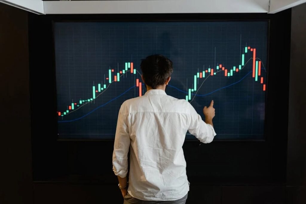 "A person is analyzing a financial graph on a digital screen, pointing at the rising and falling trends. This image reflects the importance of understanding financial patterns and planning, especially when it comes to budgeting for life after high school."