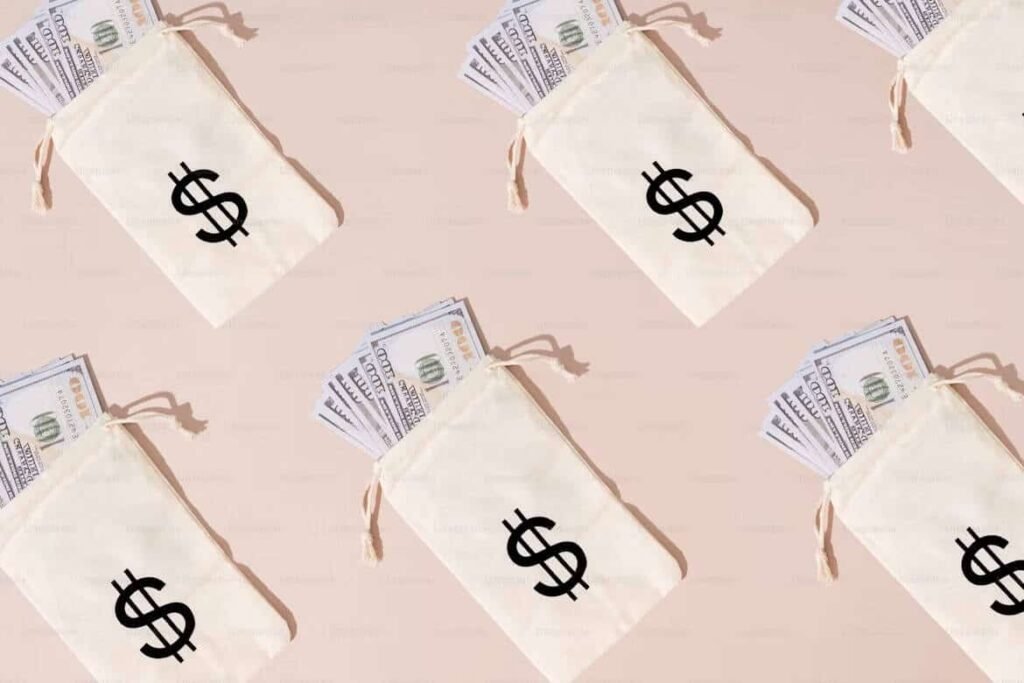 Multiple beige money pouches with bold dollar signs, each filled with stacks of U.S. hundred-dollar bills, laid out on a soft pink background. This image visually represents financial abundance and budgeting, tying into the question: how much spending a week is reasonable?—a reminder to align cash flow with smart money habits.