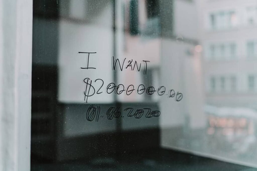 A handwritten message on a glass window reads “I WANT $2,000,000.00 – 01.06.2020,” symbolizing a strong financial goal. This reflects the mindset behind a no spending challenge, where individuals commit to saving and cutting expenses to reach ambitious money goals.