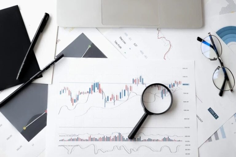 Flat lay of financial documents, charts, graphs, magnifying glass, pen, glasses, and laptop, illustrating a teenager’s budgeting and personal finance journey, learning how to manage money, track savings, and build smart spending habits