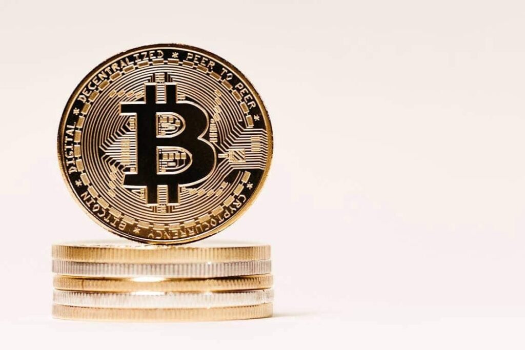 A golden Bitcoin coin stands on a stack of other coins, symbolizing a modern and smart way for teenagers to save their money.