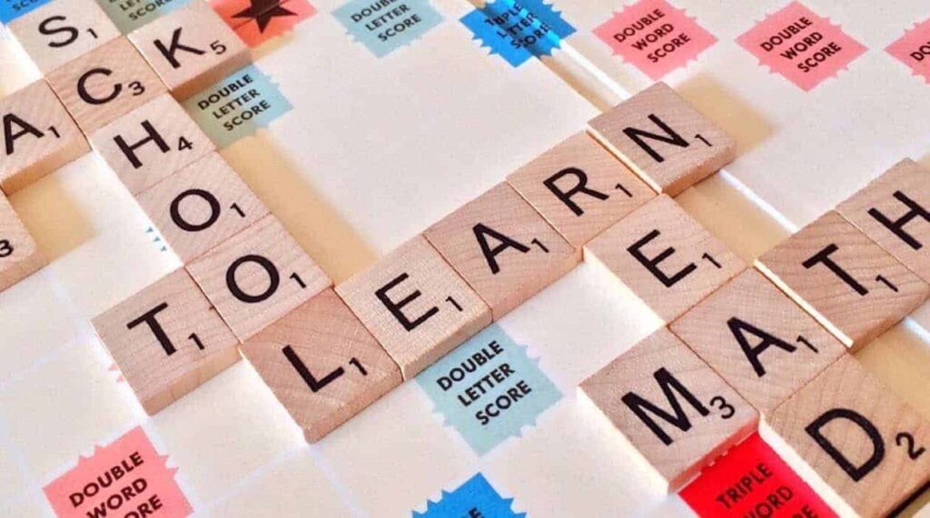 A close-up of a Scrabble board with the words "SCHOOL," "LEARN," and "MATH" spelled out. This image represents the importance of education and financial literacy for teenagers. It can be used for content discussing how to apply math and learning skills from school to successfully save money and plan for future purchases.