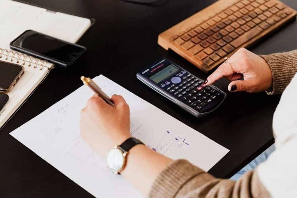 College student using a calculator and budget worksheet at desk — creating a personalized college student budgeting template for managing expenses, saving money, and planning monthly finances.