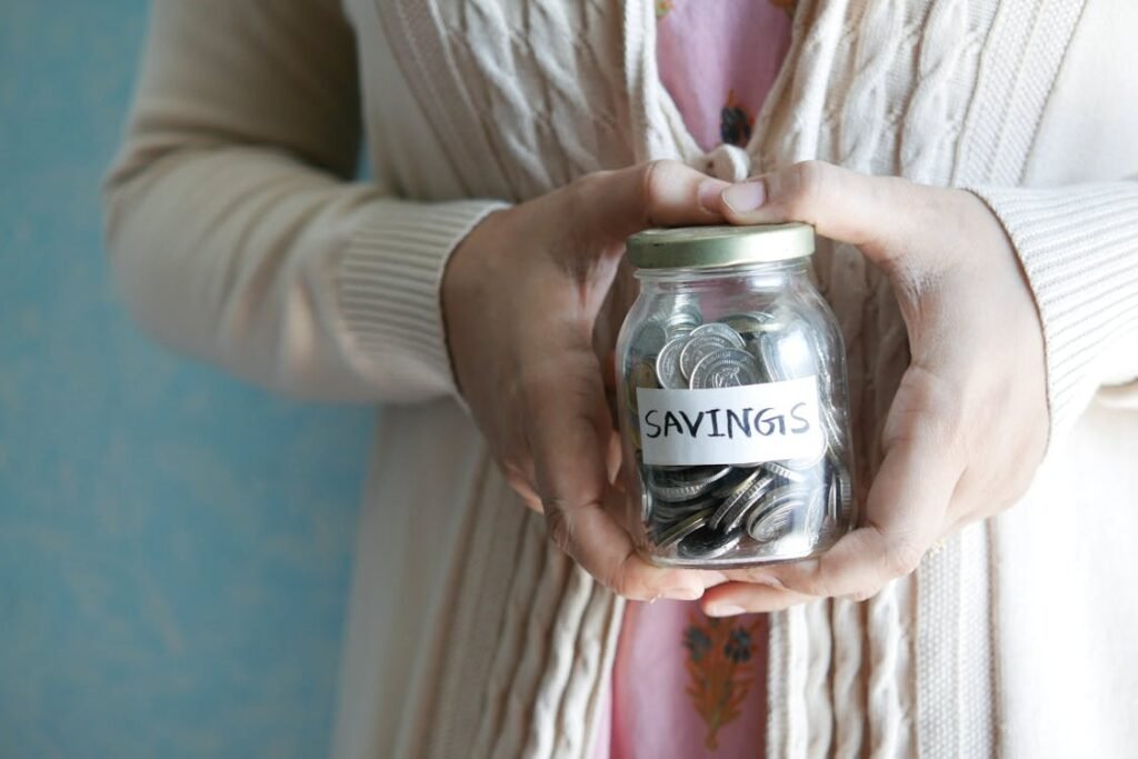 A person holding a glass jar full of coins labeled ‘SAVINGS,’ symbolizing saving money and financial planning.