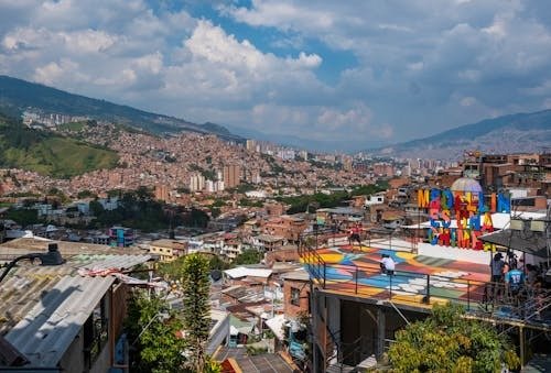 Medellín travel view of colorful hillside neighborhood, murals, and mountains in Colombia cityscape.