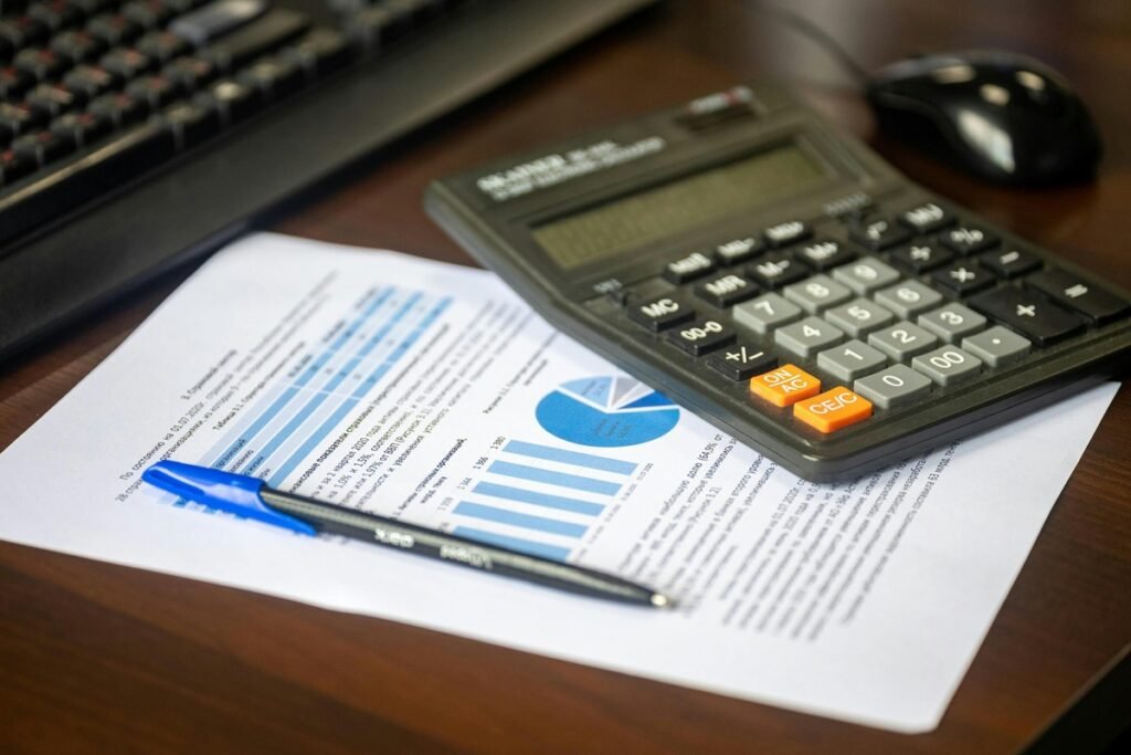 A calculator, financial charts, and a pen on a desk used for an auto loan payoff calculator to review payments and interest details.