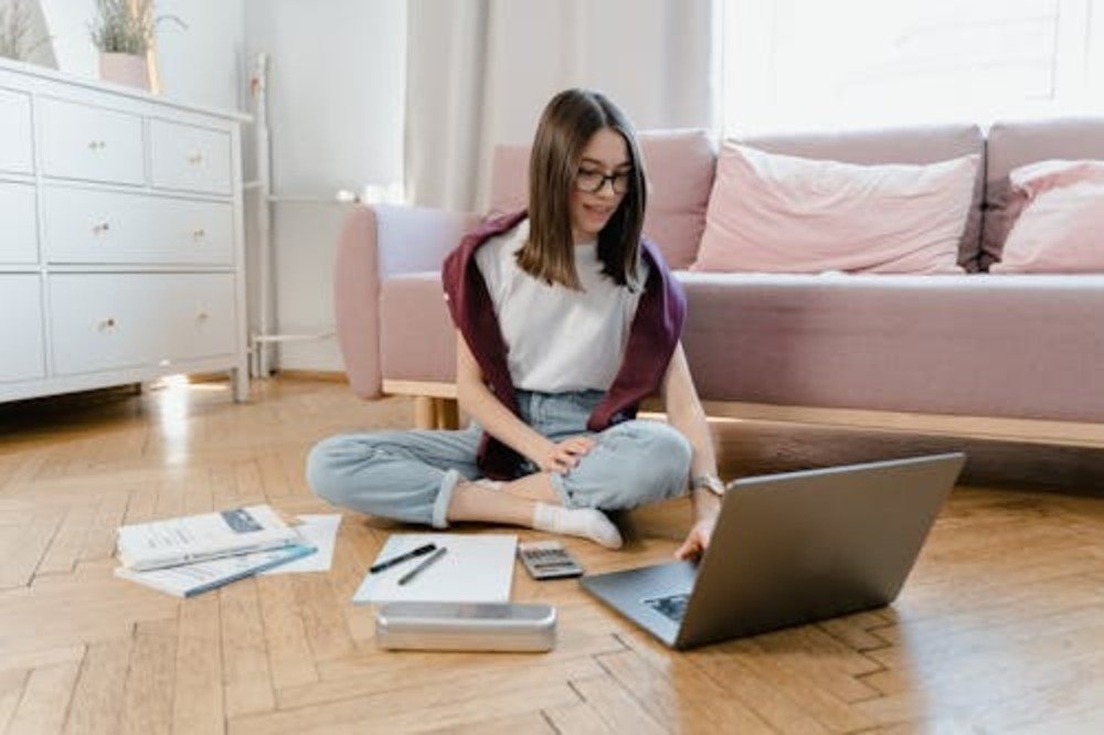Young woman sitting on the floor with laptop, calculator, and bills while planning her private student loan repayment strategy