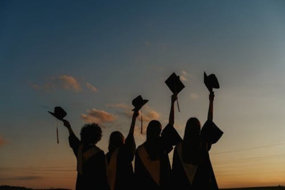 Group of graduates celebrating outdoors at sunset, symbolizing financial freedom after paying off student loans.
