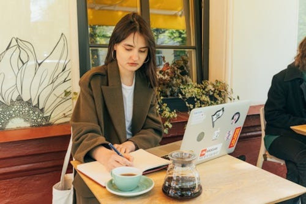 College student budgeting for apartment expenses on a laptop and notebook at a café.