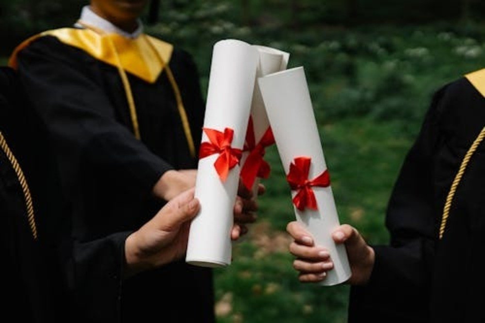 Graduates holding rolled diplomas with red ribbons after lowering tuition costs successfully