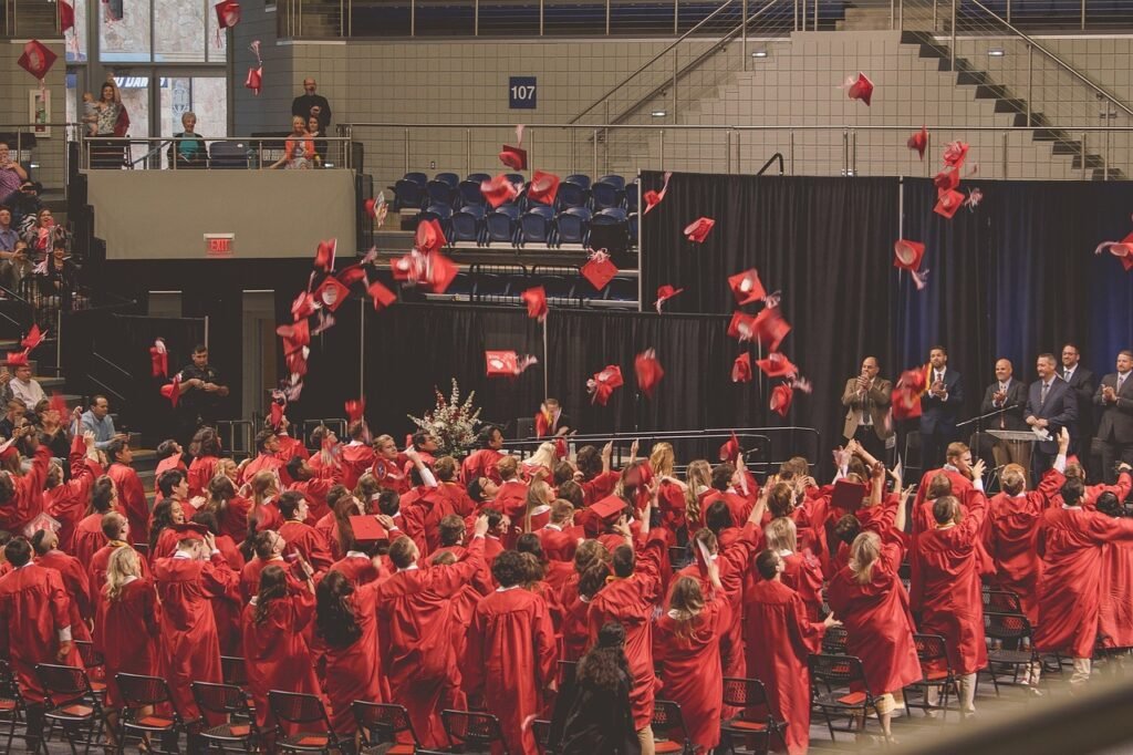 Students in red graduation gowns celebrating by tossing caps in the air during commencement ceremony.